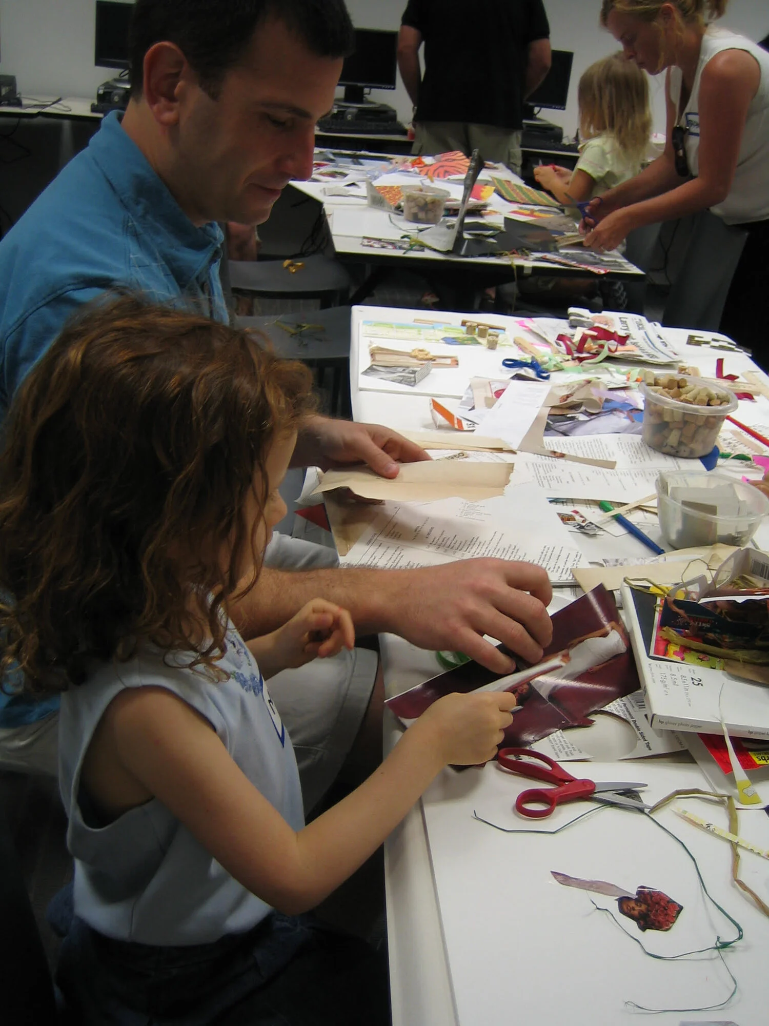 An adult and a child cutting and arranging paper together at a collage table