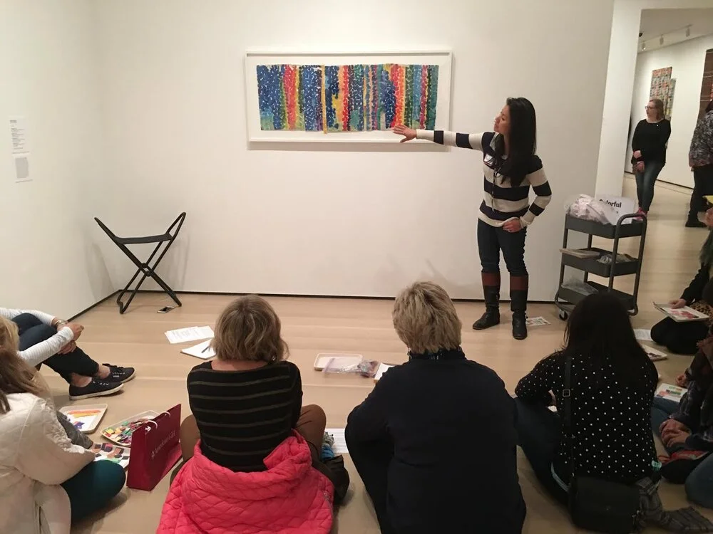 An educator points to a work of art while a seated group looks on