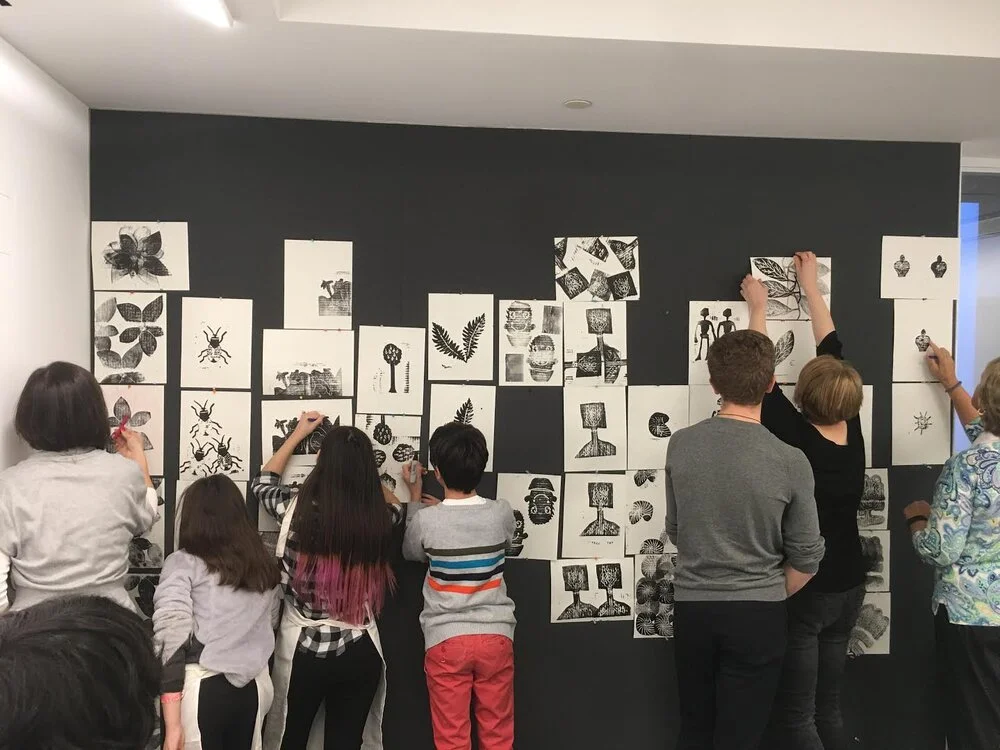 Students and adults pinning black and white prints across a dark gallery wall