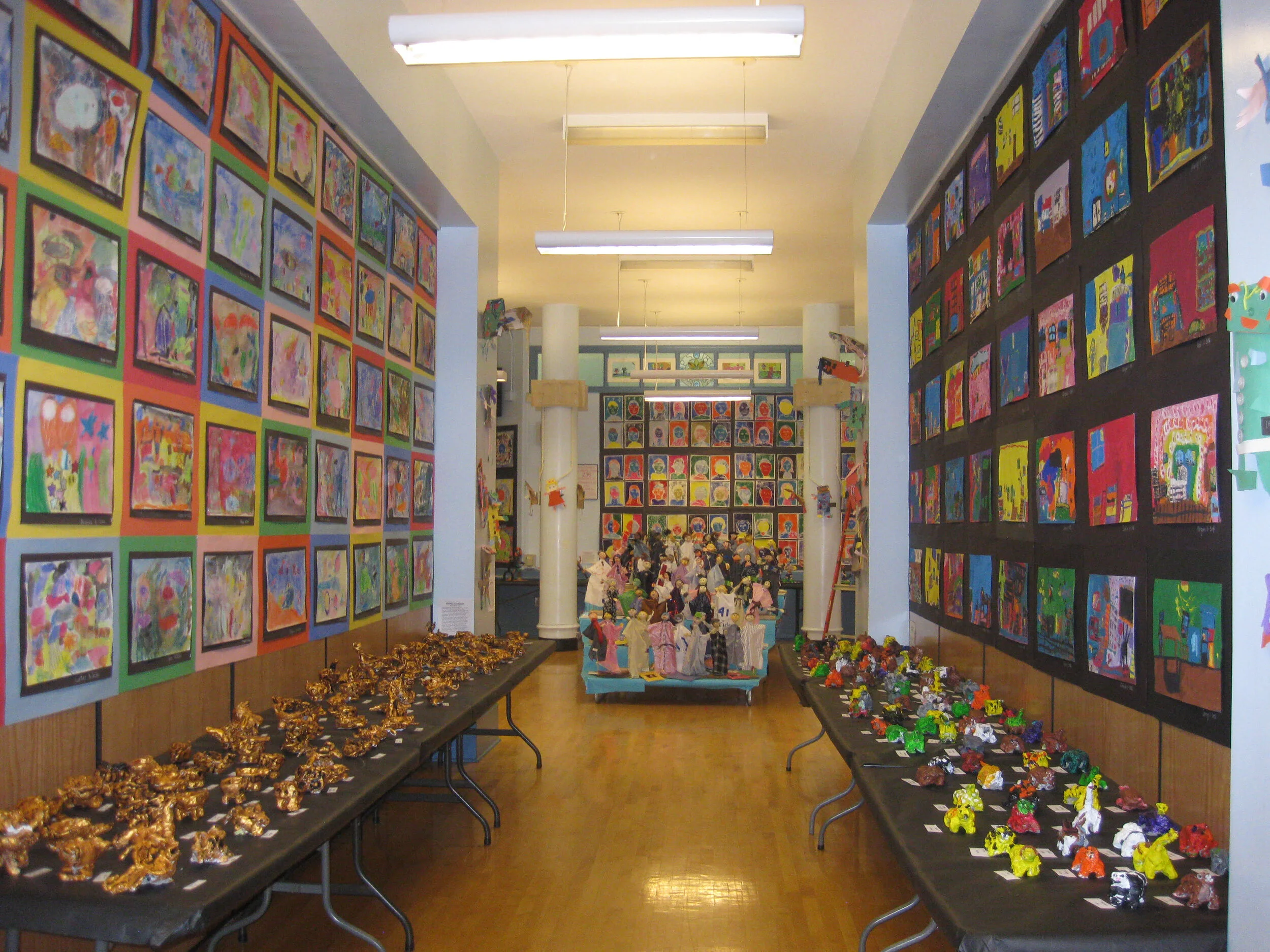 A school hall lined with student paintings and tables of painted clay sculptures